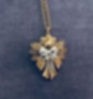 A decorative gold-toned angel pendant set against a maroon background.