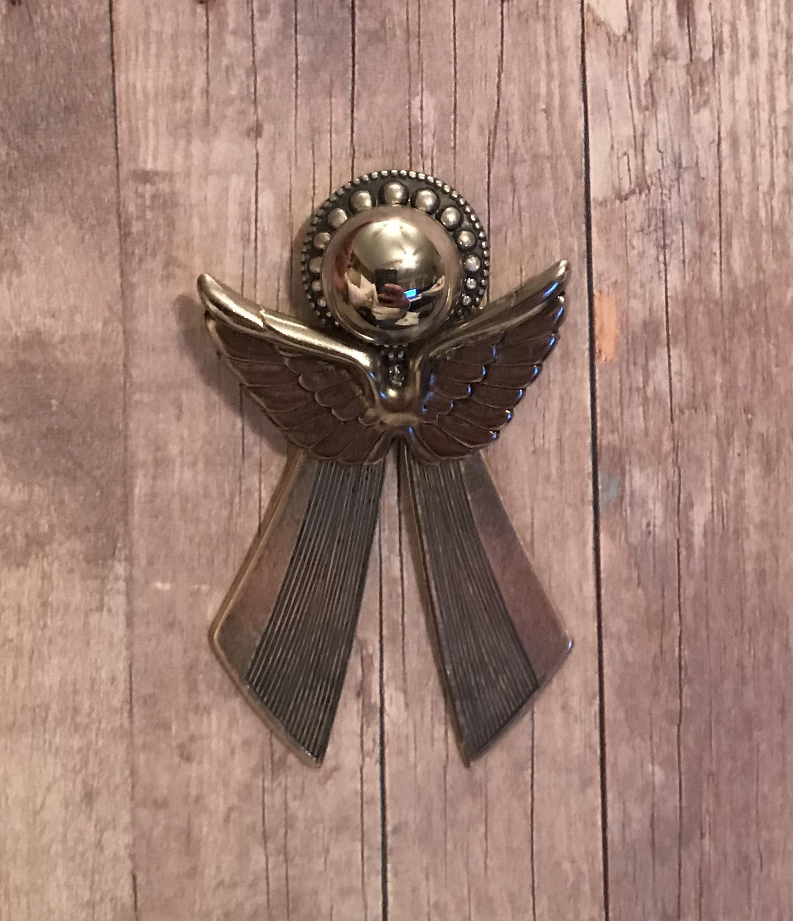A gold male angel pin on a wood look background.