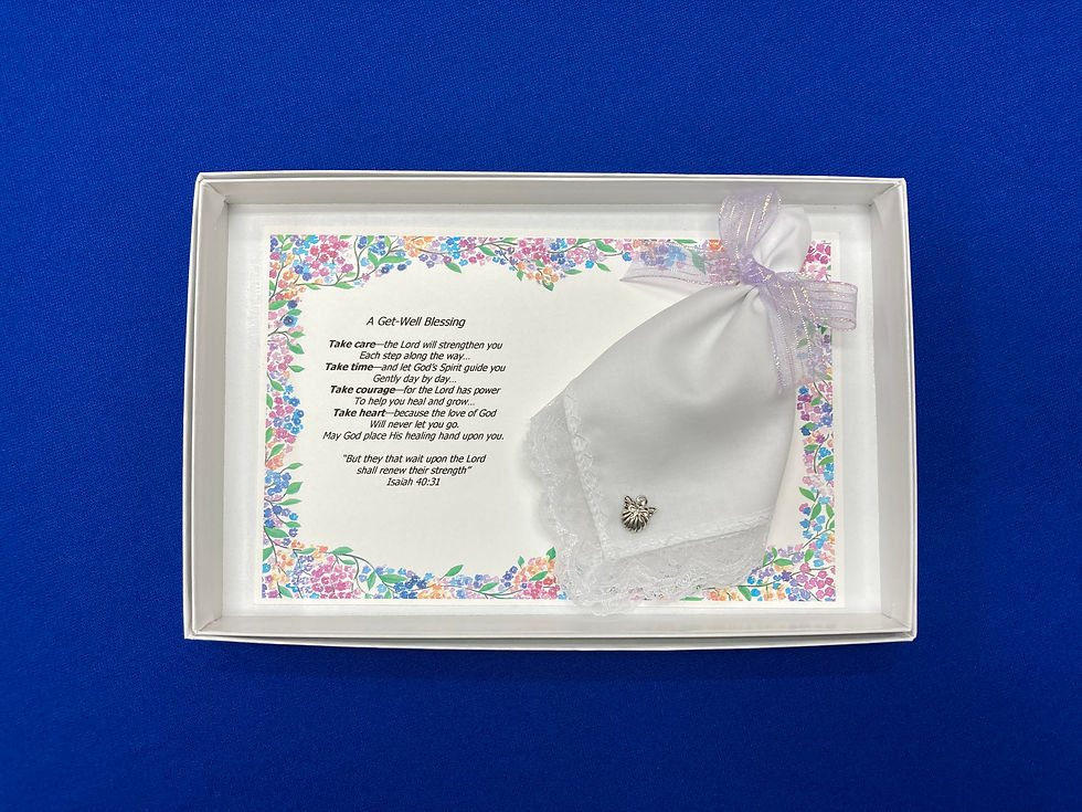 A white box with a card with a floral border and a printed poem, alongside a white hankie adorned with an angel pin.