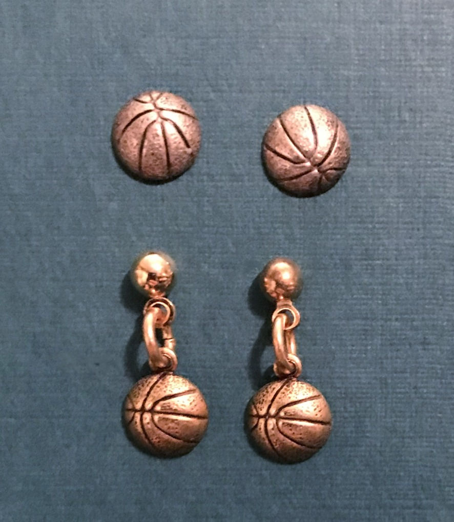 Thumbnail: Two pair of tiny basketball earrings, one silver, one gold, on a dark green background.