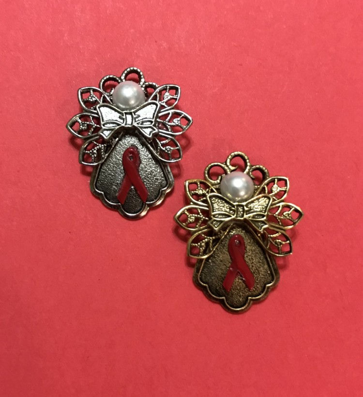 Thumbnail: A Silver and a gold angel pin with red cancer ribbons on the skirts on a red background.