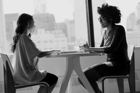 two ladies sitting down at a table talking to eachother