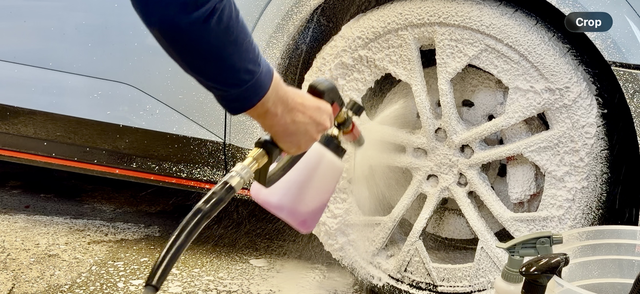 A professional car wheel cleaning session featuring thick cleaning foam applied to a luxury alloy wheel.