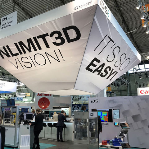 Moderner IDS-Messestand mit Schwerpunkt auf 3D-Vision-Technologien, klar strukturiert mit zentralem Info-Desk und LED-Display