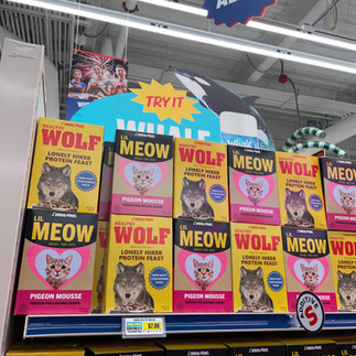 Colorful boxes of parody cat food labeled “Meow Wolf” stacked on a grocery shelf inside Omega Mart at AREA15 Las Vegas.