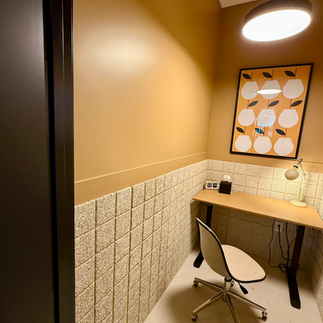 Private phone booth workspace with warm lighting, tan tiled wall, and minimalist desk setup.