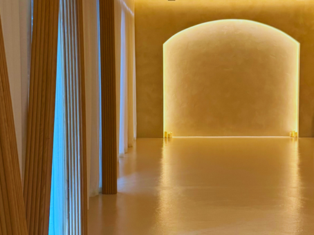 Minimalist yoga studio interior at Kintsugi Yoga in Las Vegas featuring soft golden lighting, smooth beige flooring, and vertical wood panel accents.