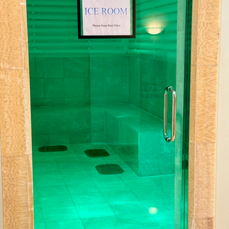 The Ice Room at Imperial Spa Las Vegas, illuminated with green lighting, showing tiled bench seating and a glass door marked with a sign reading “ICE ROOM – Please Keep Door Closed.”