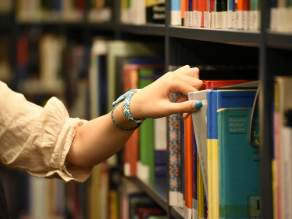 A person holding a book in the foreground… but the focus is not on the book—it’s on the person behind it.