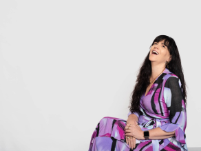 Justine Martin in a colorful purple dress sitting and laughing joyfully, radiating authenticity and empowerment through her presence and story.