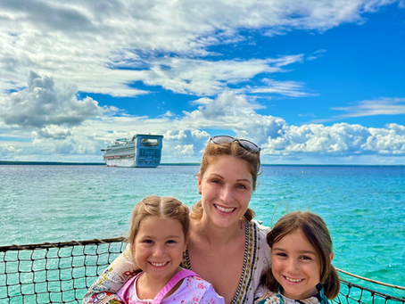 A woman and two children with water and a cruise ship in the background