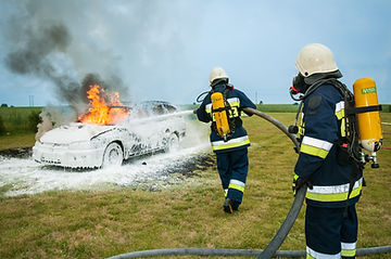 Two firefighters using foam to suppress a flaming car