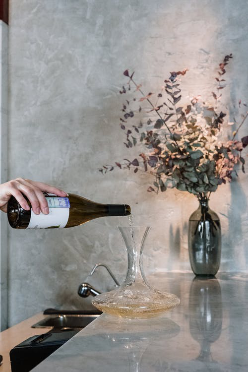 A person is pouring white wine in a crystal decanter to aerate the drink.