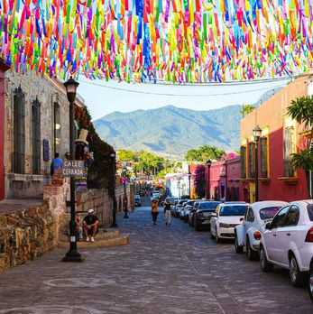 Colorful streamers hang over the cobblestone streets of the Xochimilco neighborhood of Oaxaca de Juarez, México, as tourists walk by