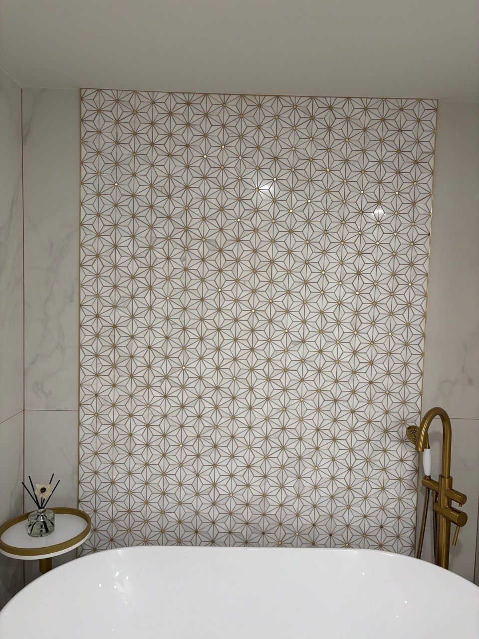 Elegant bathroom with patterned wall and gold fixtures.