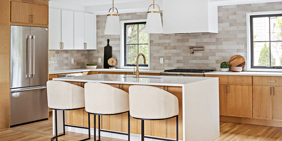 Modern kitchen with wood cabinets, marble island, and beige chairs. Stainless steel fridge. Bright with large windows and pendant lights.