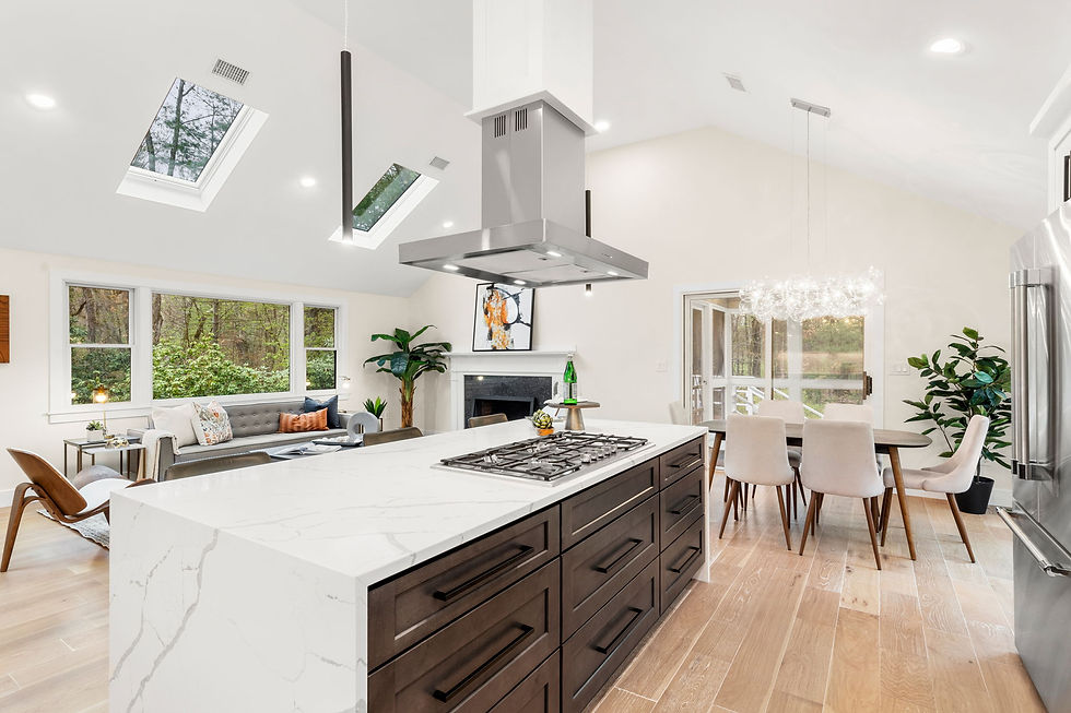 Modern kitchen with a marble island, dark cabinets, gas cooktop, and light wood floor. Skylights, greenery, dining area, and a cozy seating nook.