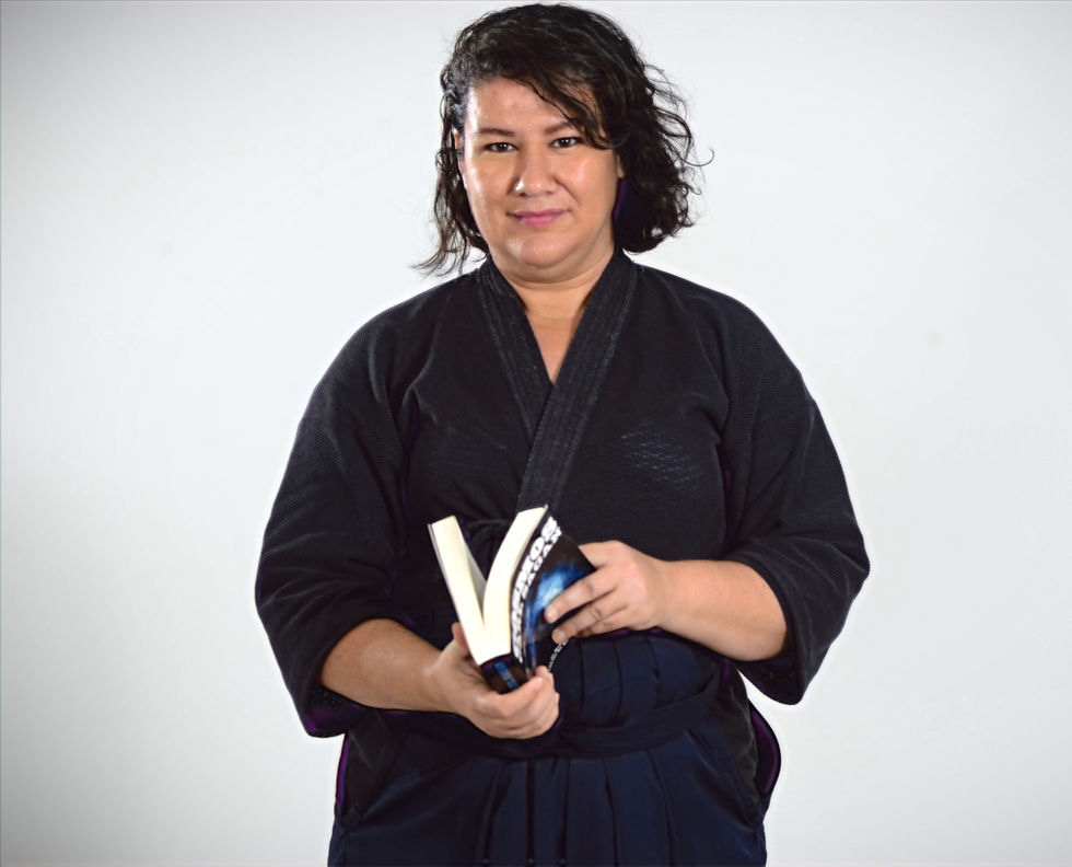 Sensei Irenilda Medeiros em pé, vestida com um kimono roxo e segurando um livro.