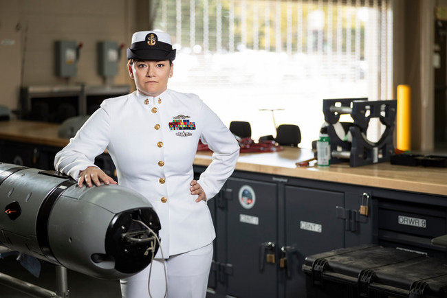 US Navy Sailor female in Service Dress Whites in a workshop, serious expression. US Navy Uniform Guide