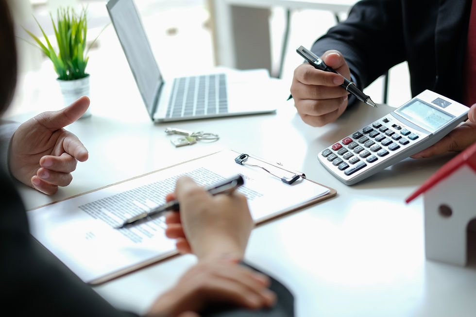 Meeting at a white desk with a laptop, calculator, contract papers and pens as people discuss finances.