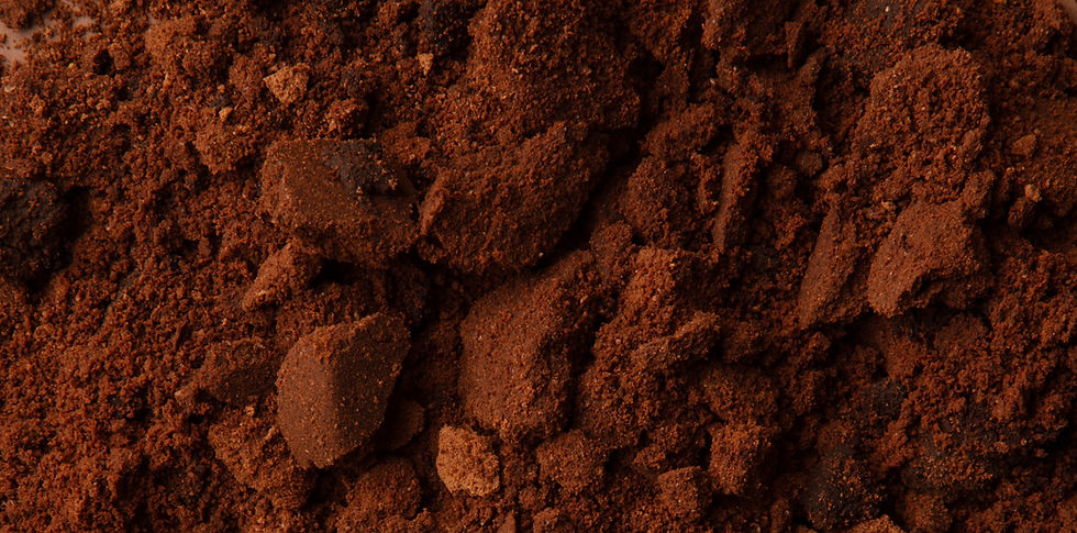 A close-up image of used coffee grounds, showcasing their rich, dark brown color and coarse texture with small clumps and particles.