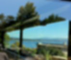 View Through A Large Bay Window To The Puget Sound and Beautiful Green Forested Hills With Mountains In The Background.