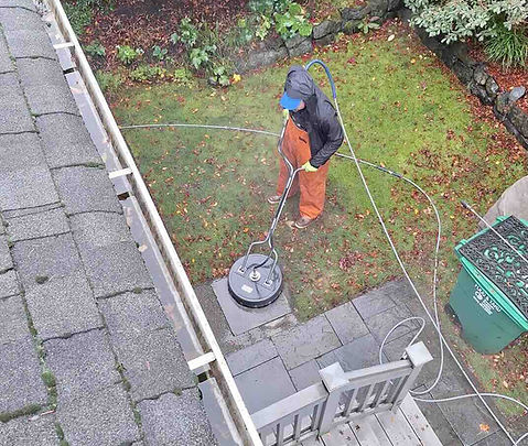 Husser technician using a surface cleaner to power wash stone paver patio stones in the backyard