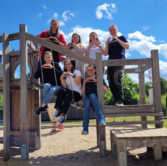 7 Jugendliche von der Johanniter-Jugend auf einem Spielplatz, alle formen ein Herz mit den Händen