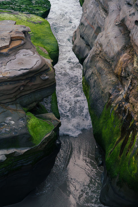 above perspective of wave channel between two large sandstone rocks with waves crashing between.