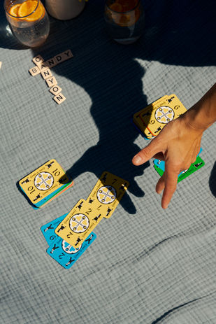 a hand throwing down a card in a game on a blue muslin blanket with hotel name in banana grams