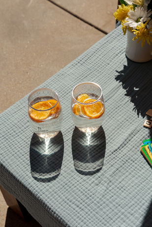 cabana at hotel pool, image of two glasses of bubbles with orange garnishes sitting on blue muslin blanket with flowers off the side