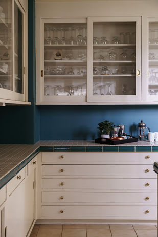 interior image of vintage butler's pantry with tiled countertops and glass paneled cabinets above, blue paint backsplash