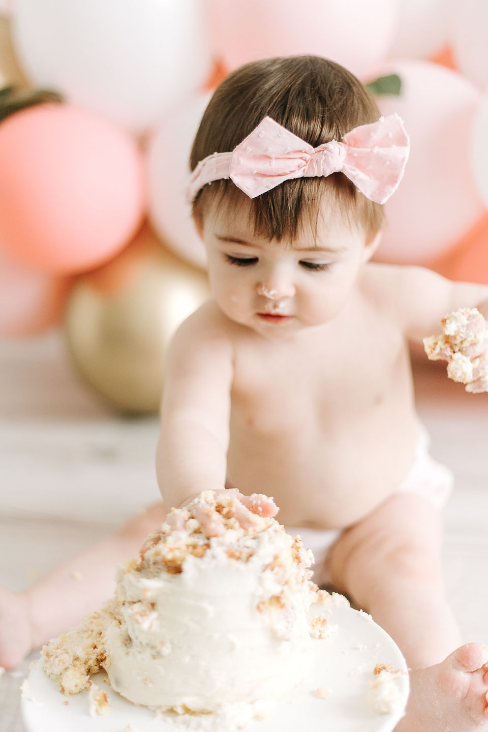 A one year old sits behind a small cake and puts her hands in it
