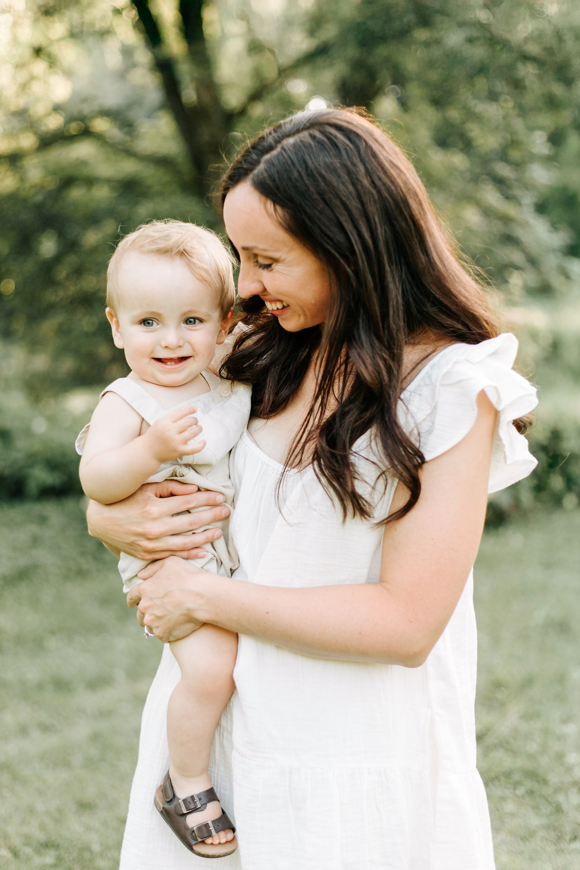 A woman in a white dress holds a boy in her arms and smiles at him