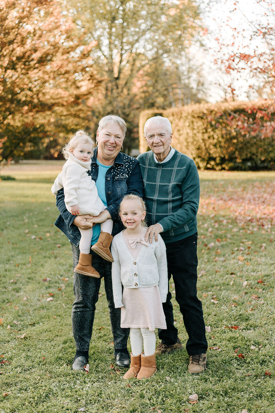 An older couple stand with the woman holding a young girl in her arms as another young girl stands in front of them