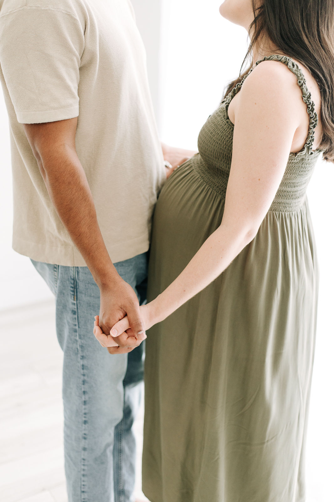 torso of a woman in green dress and pregnant stomach holding hands with a man in jeans and a t shirt