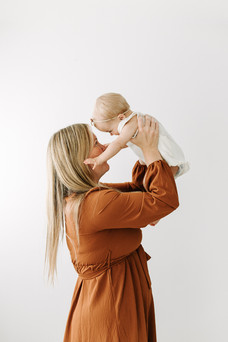 A woman lifts a one year old girl into the air