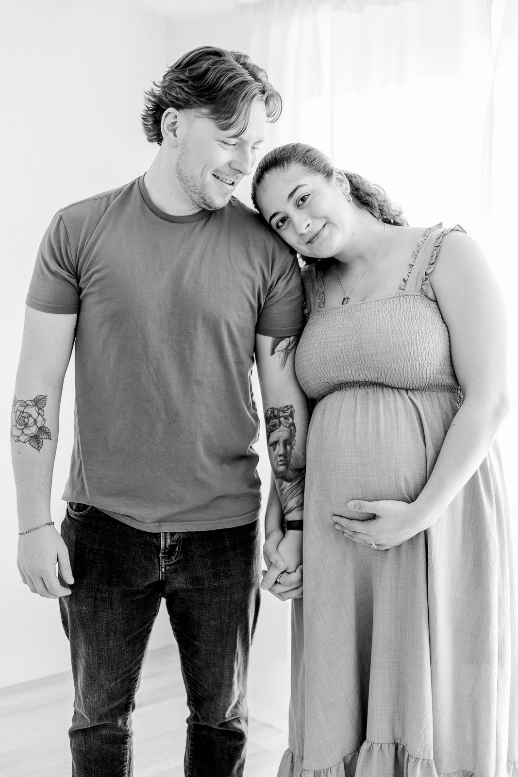 black and white image of a man standing and holding hands and looking down at a pregnant woman who is cradling her pregnant belly