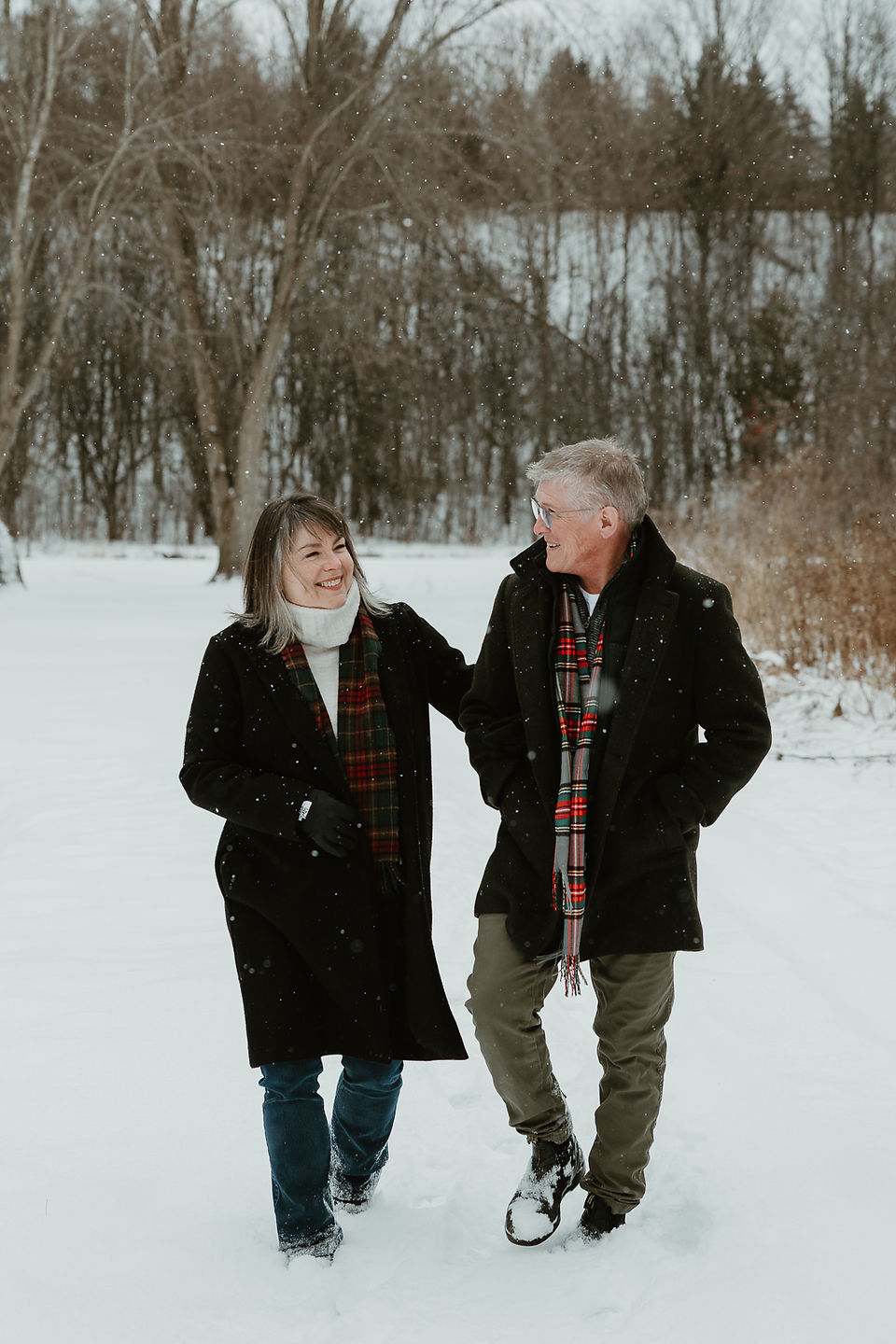 An older couple walk arm in arm and look at each other smiling in the snow