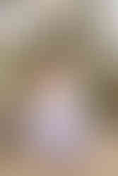 A woman in a blue dress sits on a small wooden bench with a young girl on her lap who is laughing as they are surrounded by a large floral arrangement