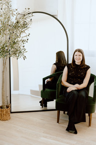 A woman sits in a green chair in front of a large mirror