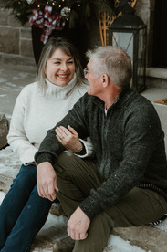 An older man and woman sit on a doorstep in winter and look at each other smiling