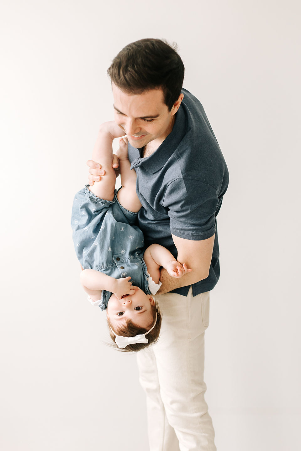 A man holds a one year old girl in his arms and holds her upside down