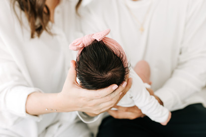 A newborn baby rests in a man's arms while a woman cradles the baby's head