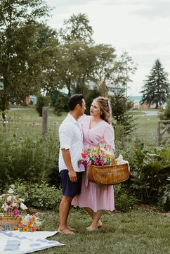 A woman holds a basket with flowers and stands next to a man in a field
