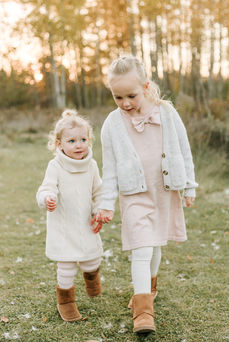 Two girls walk hand in hand on a grass path amongst trees in the fall