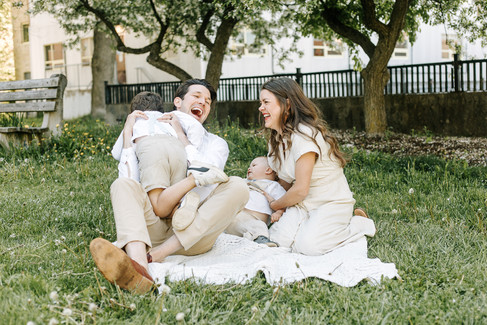 A man and woman sit on a blanket and laugh as they play with two boys