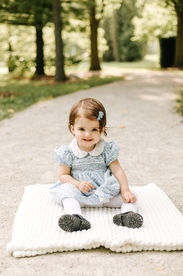 A young girl sits on a blanket on a path under trees