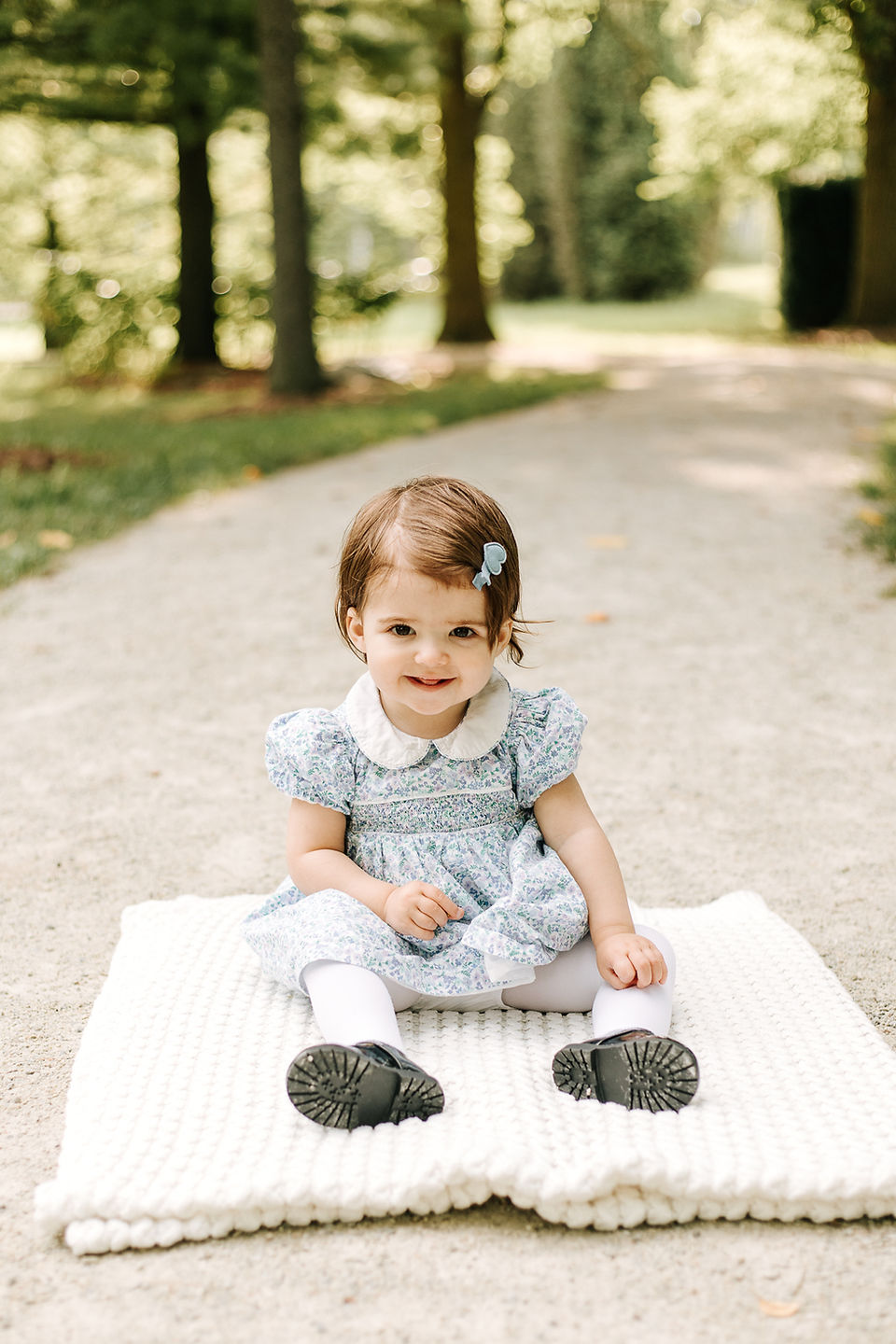 A young girl sits on a blanket on a path under trees