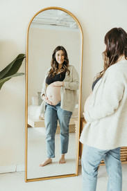 A pregnant woman stands in front of a mirror and rests her hands on her pregnant stomach